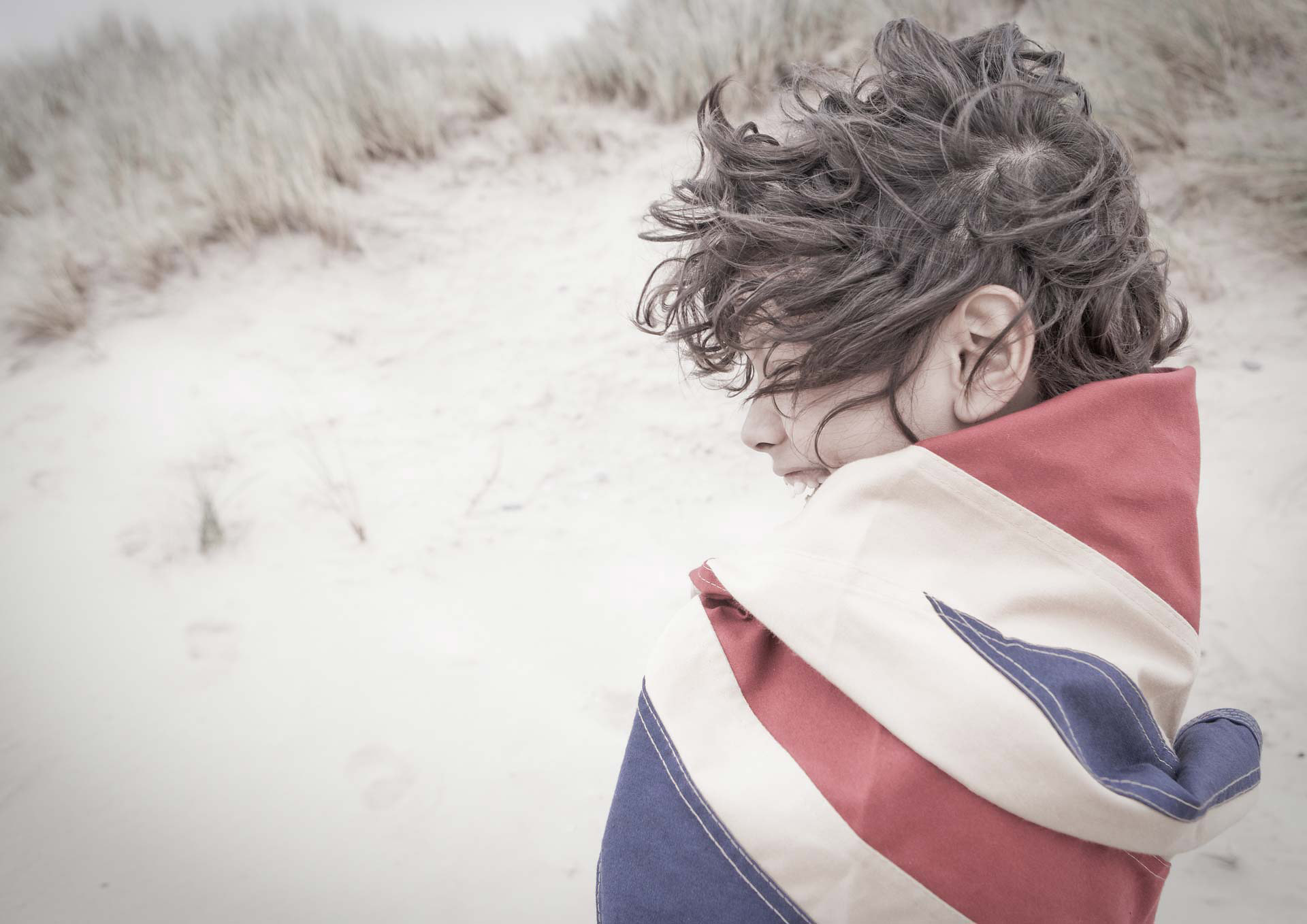 A child standing on a windy beach, turned away from the camera