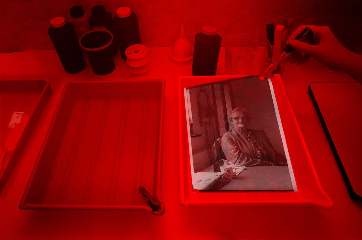 A photographic print being developed in a darkroom tray under red safelight.
