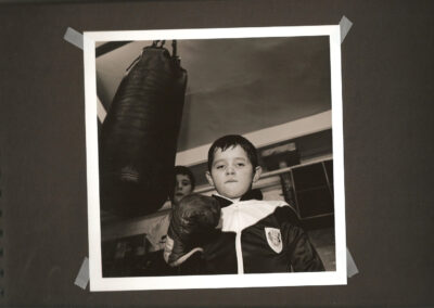 Young boy in a boxing gym framed by other boys and activity around him.