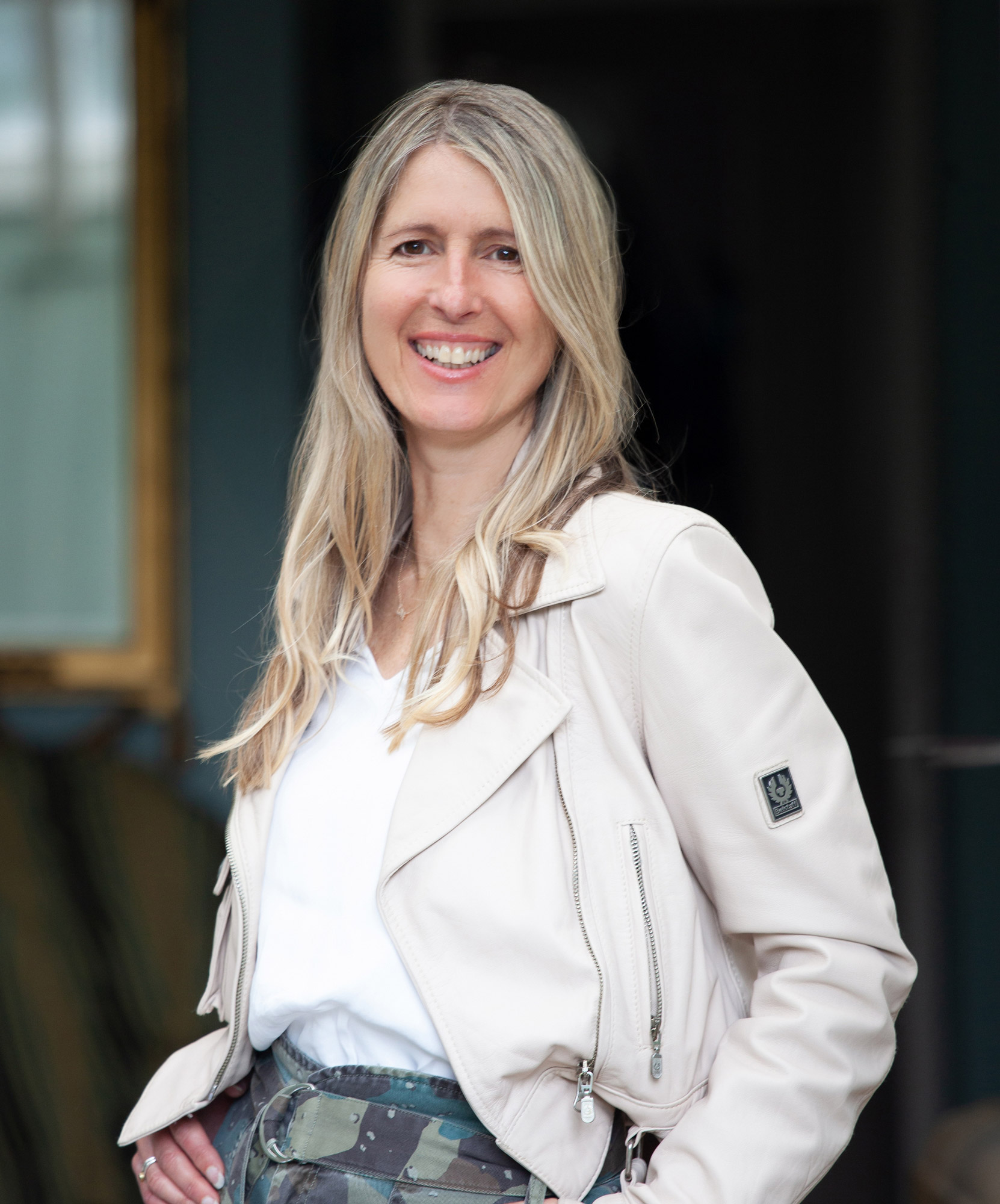 Portrait of fine art and documentary photographer Tamara Peel, smiling, wearing a soft neutral jacket and white top, photographed in natural light.