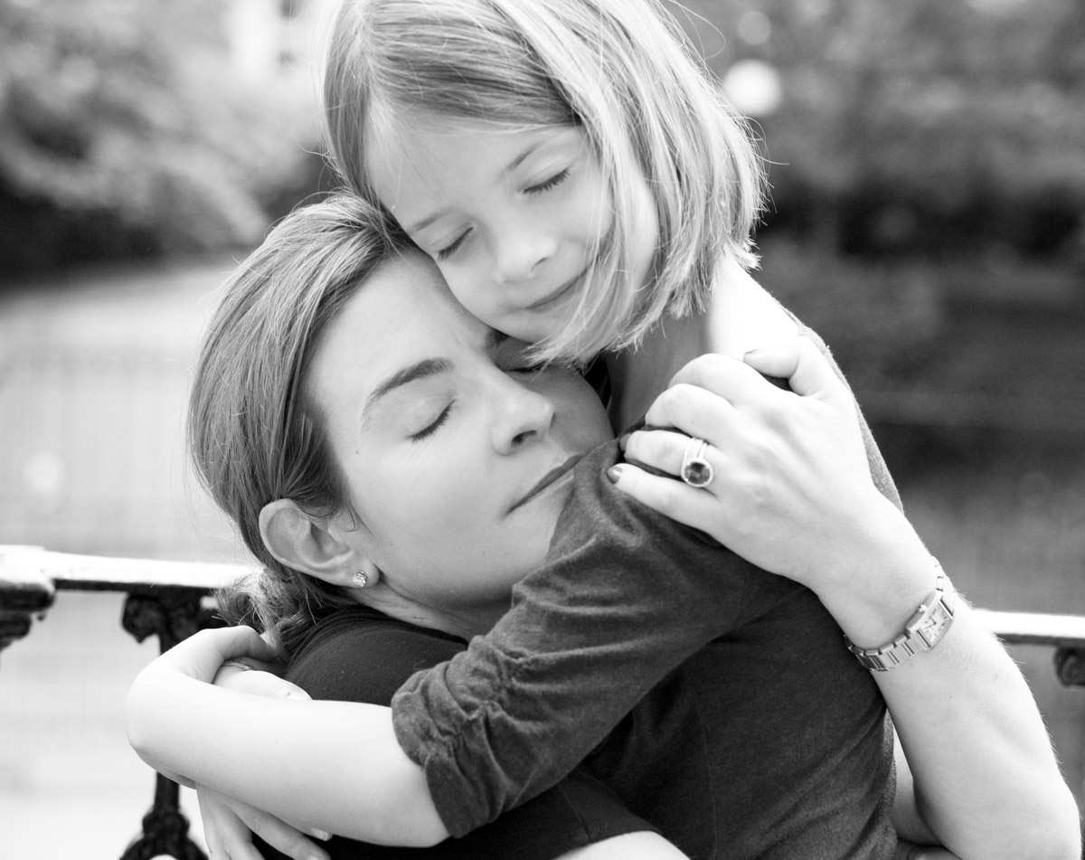 Black and white photograph of a mother holding her young child, both with eyes closed, sharing a quiet moment of closeness.
