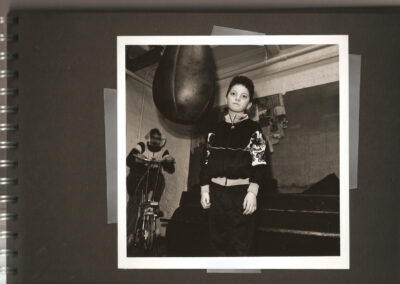 Young boy standing beneath a hanging boxing bag inside a community boxing gym.