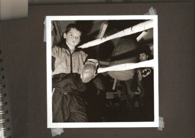 Young boy training in a boxing gym, practising movements near a bag and ropes.