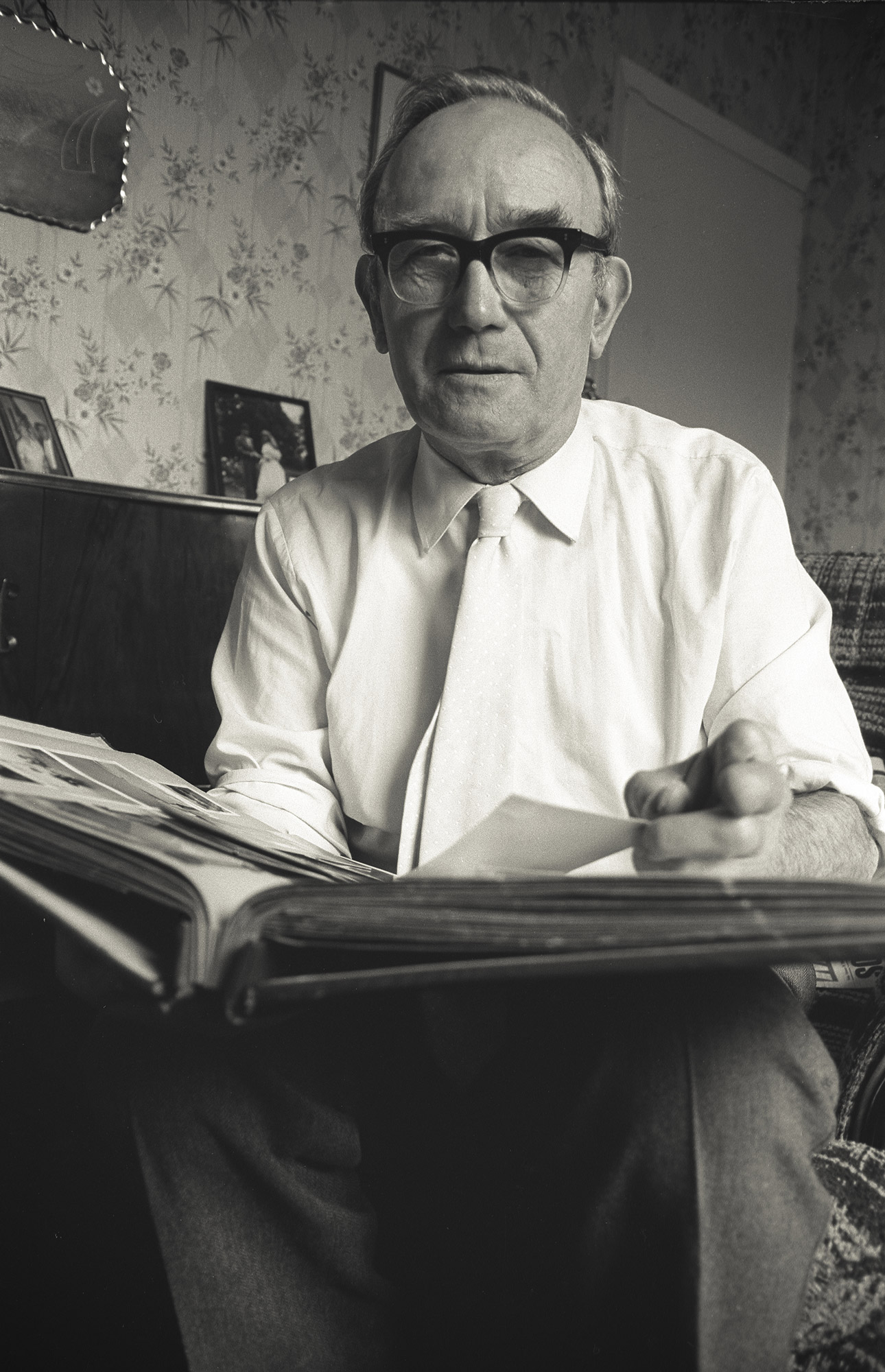 An elderly man holding and looking through family photographs, surrounded by albums and prints.