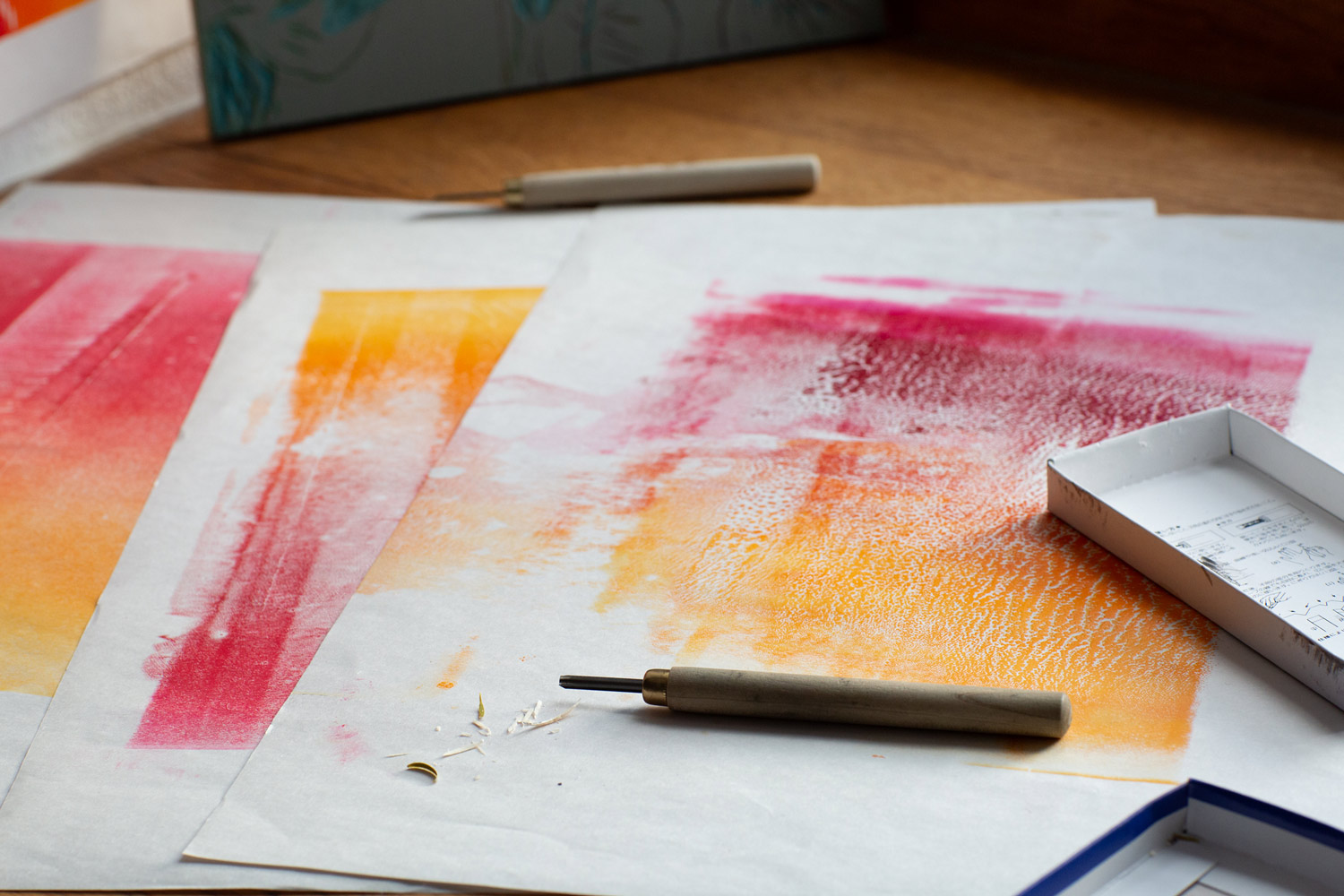 Printmaking cutting tools and coloured ink rolled onto test paper during an experimental printing process.
