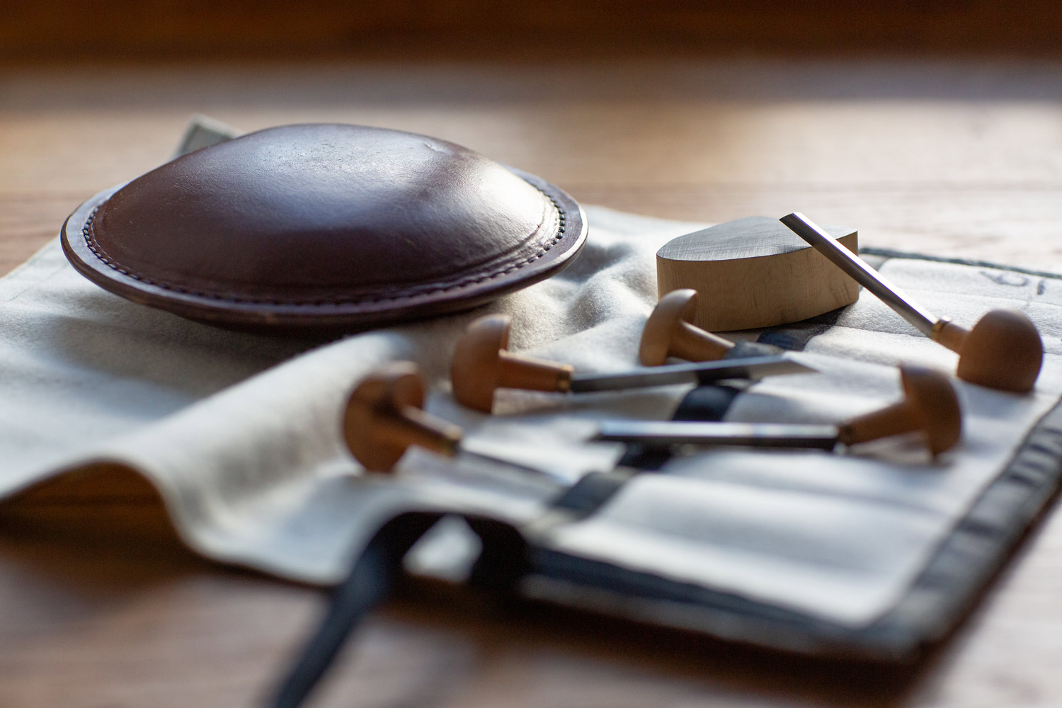 Woodcut tools, a leather turning circle, and a small wooden block arranged on a work surface.