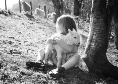 Girl sitting beneath a tree holding a lamb in her arms, both resting quietly.