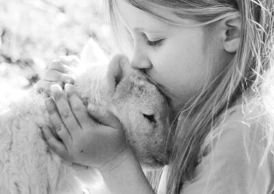 Girl kissing a newborn lamb on a family farm in Mid Wales, photographed in black and white.